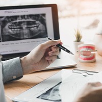 Dentist and patient at desk with X-rays and toy teeth discussing treatment plan