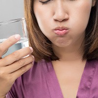 Woman in purple shirt with eyes closed rinsing mouth with water