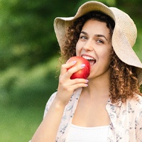 Woman in straw hat with dental implants in Owings Mills, MD eating an apple
