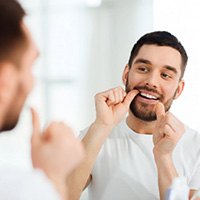 Man flossing his teeth in mirror
