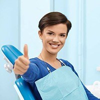 Smiling young woman in dental chair giving thumbs up 