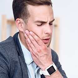 Man grimacing holding cheek in pain