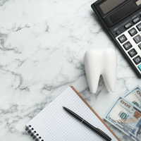 Bird’s eye view of notebook, pen, money, model tooth, and calculator on marbled surface