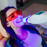 Woman in dental chair in protective goggles with UV light on teeth