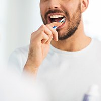 Man in white t-shirt brushing teeth at mirror