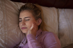 Woman in bed holding jaw in pain 