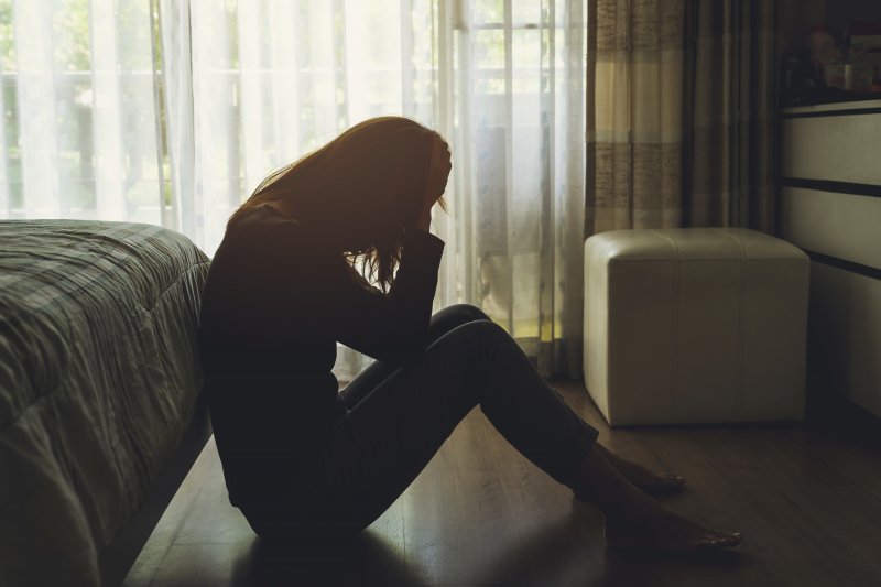 A lonely young woman sitting next to her bed while feeling depressed