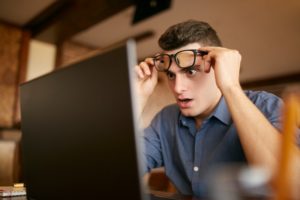 man looking surprised while reading laptop