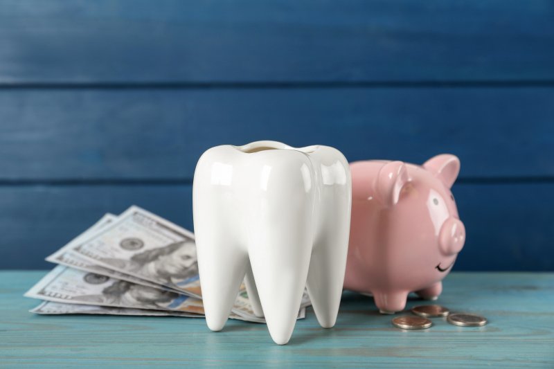 A large ceramic tooth next to a piggy bank and some money