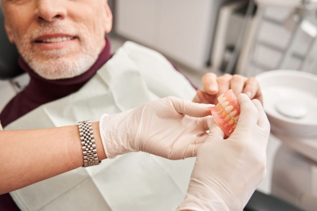 A man in a dental chair holding dentures